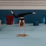 A female gymnast skillfully performs a handstand in an indoor gymnastics training facility.