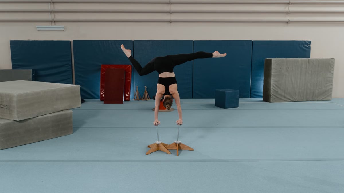 A female gymnast skillfully performs a handstand in an indoor gymnastics training facility.