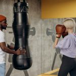 A woman practicing boxing with a coach in an indoor gym setting, focused on a training session.